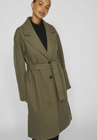 Olibu zaļš garš mētelis, izgatavots no mīkstas auduma, ar izgriezumu apkakli, vienu pogu aizdari un saskaņotu jostu viduklī.