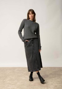 Szary prążkowany sweter, wysoki dekolt, połączony z długą czarną spódnicą dżinsową. Czarne buty na sznurówki i skarpetki dopełniają strój.