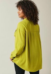 Langærmet bluse i klar limegrøn, med en afslappet pasform, blød tekstur og knappeaccentuer på manchetterne. Glat, flydende design.