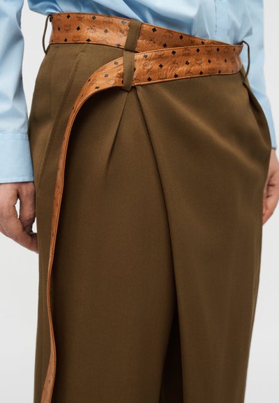 Homme portant un pantalon plissé marron avec une chemise bleu clair et une large ceinture en cuir beige ornée d'un motif losange noir.