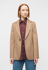 Καφέ σακάκι με ομαλή υφή, με ένα κουμπί και δύο μπροστινές τσέπες, συνδυασμένο με πουκάμισο μπορντό με ρίγες και μπλε τζιν.