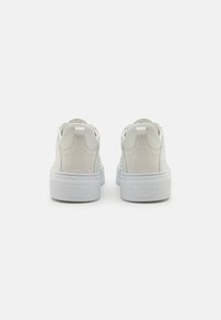 Baskets blanches en cuir lisse et texturé, avec une semelle en caoutchouc solide, au design minimaliste et une branding subtile sur le talon.