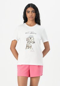T-shirt en coton blanc avec un motif d'un chien tacheté portant une couronne et un collier. Associé à un short rose. Texte superposé inclus.