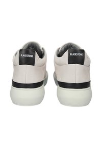 Vita lädersneakers med en svart hälla märkt "BLACKSTONE." Har en slät yta, minimalistisk design och en tjock vit sula.