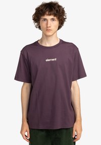 Camiseta corta de manga en color púrpura, fabricada en algodón, con un logo frontal en un color que contrasta. Corte relajado con un escote redondo.