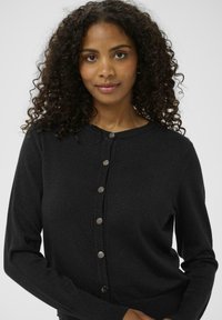 Schwarze Strickjacke mit rundem Ausschnitt, langen Ärmeln, vorderem Knopfverschluss und einem subtilen Schimmer in der Strickstruktur.