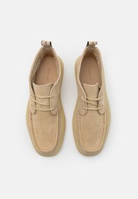 Paire de chaussures à lacets en daim beige avec bouts carrés arrondis et semelles en crêpe, vue de dessus sur fond blanc.