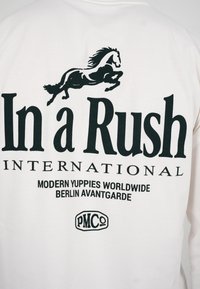 Gráfico negro de un caballo galopando sobre un texto grande que dice "In a Rush" con textos más pequeños "International", "Modern Yuppies Worldwide Berlin Avantgarde" y un logo "PMCo".