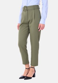 Pantaloni tailored verde oliva con cintura larga, pieghe frontali e taglio cropped. Indossati con una camicia a maniche lunghe blu chiaro e tacchi neri.