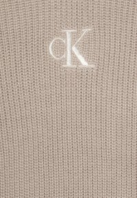 Beez värvi kootud sviiter, millel on tekstuurne kangas ja esiküljel väike valge brodeeritud 'cK' logo. Pehme ja kerge materjal.