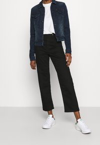 Tmavě modrá džínová bunda s límečkem, dvěma náprsními kapsami a knoflíky; spárovaná s černými kalhotami s vysokým pasem a bílými teniskami.