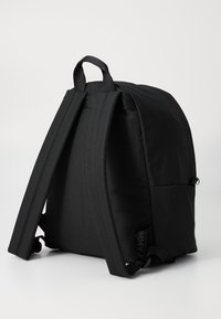 Zaino nero con spallacci imbottiti e maniglia superiore. Tessuto liscio e resistente con una forma strutturata e un branding discreto sul lato.
