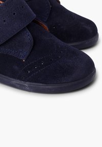 Zapatos de ante azul marino con tiras de velcro, que presentan patrones perforados en la parte superior y una suela de goma texturizada para mayor agarre.