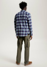 Camicia a quadri in blu, rosso e bianco, con colletto a camicia. Abbinata a pantaloni cargo color oliva con tasche laterali.
