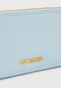 Φωτεινό γαλάζιο πορτοφόλι με υφή δερμάτινου τελειώματος, χρυσά εξαρτήματα και ανάγλυφο λογότυπο «LOVE MOSCHINO» στο μπροστινό μέρος. Λεπτομέρεια με φερμουάρ κλεισίματος.