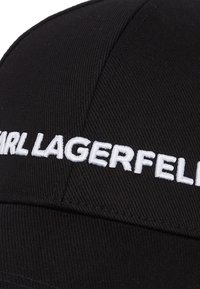 Svart caps med hvit brodert logo "KARL LAGERFELD." Laget av teksturert stoff med en strukturert form og buet skjerm.