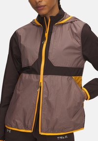 Lightweight zip-up jacket in brown, featuring a hood, bright orange accents, and contrasting panels. Smooth texture with two front pockets.