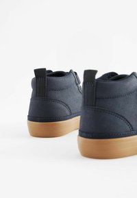 Ciemnoniebieskie tekstylne buty o gładkim wykończeniu, z brązową gumową podeszwą i tylną pętlą do zakupu. Cechują się minimalnym przeszyciem, co nadaje im elegancki design.