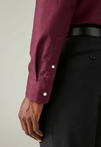 Cămașă bordo cu mansete cu nasturi, din material din bumbac, textură netedă, asortată cu pantaloni negri croiți, având un detaliu cu nasturi.