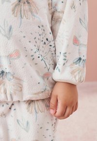 Pehmeä fleece-setti vaaleanpunaisena, jossa on kukka- ja pupukuoseja. Joustoarvot, teksturoitu kangas ja rento istuvuus mukavuutta varten.