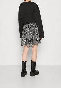 Sweatshirt oversized noir, jupe plissée noire et blanche à motifs, et bottes noires montant jusqu'aux genoux avec semelles épaisses.