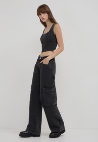 Top corto nero con borchie testurizzate abbinato a pantaloni cargo neri a gamba larga con tasche laterali e una vestibilità ampia. Scarpe con platform nere.
