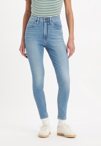 Jeans pitillo de mezclilla azul claro de talle alto con una textura suave, que presentan el clásico estilo de cinco bolsillos y un sutil desgaste.