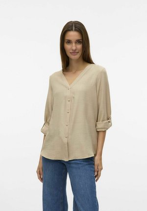 Beige, lightweight, V-neck blouse with three-quarter sleeves. Features button closure and rolled sleeve cuffs. Worn with blue denim jeans.