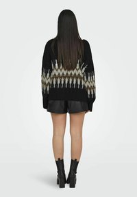 Schwarzer Strickpullover mit einem weißen und braunen geometrischen Muster, kombiniert mit schwarzen Leder-Shorts und Absatz-Ankle-Boots.