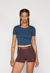 T-shirt cropped azul escuro com decote redondo, combinado com calções Nike Pro castanhos. Os calções apresentam uma faixa elástica com marca e uma textura suave.