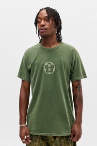 Oliwkowy bawełniany t-shirt z okrągłym dekoltem, krótkimi rękawami i centralnym dekoracyjnym wzorem w jasnym kolorze. Noszony z wzorzystymi spodniami.