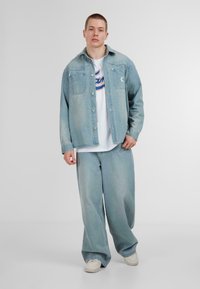 Light blue denim jacket with button closures and two chest pockets, paired with matching loose-fit jeans and a white t-shirt beneath.