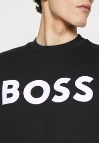 Sudadera de algodón negra con un cuello redondo acanalado y un gran logotipo en blanco "BOSS" en la parte delantera, que muestra una textura suave.