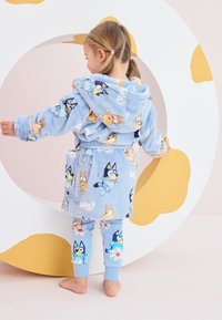Accappatoio blu di morbido tessuto con stampe di personaggi e leggings abbinati blu con fiori e cani. Tessuto soffice, design con cappuccio e tasche.