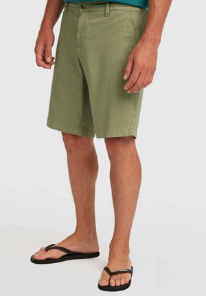 Oliwkowozielone bawełniane szorty o prostym kroju, z przednimi kieszeniami i zapięciem na guziki, zestawione z czarnymi klapkami. Prosty design i faktura.