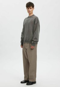 Grauer Strickpullover mit gerippten Bündchen, kombiniert mit beigen, weit geschnittenen Hosen und schwarzen Loafers. Schlichtes Design, leichtes Material und lockere Passform.