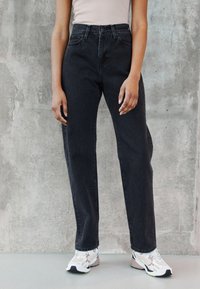 Svarte høytalede jeans med rett ben-design og detaljerte sømmer. Kombinert med hvite og beige joggesko.