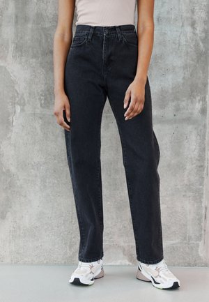 Black high-waisted jeans with a straight-leg design and detailed stitching. Paired with white and beige athletic sneakers.