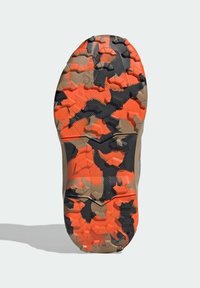 Gummisåle med et flerretningstred mønster i oransje, svart og beige. Har vinklete seksjoner for grep og stabilitet.