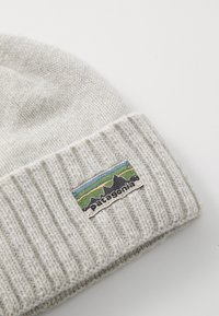 Bonnet en tricot gris avec une texture côtelée et un revers, arborant un patch brodé coloré avec le logo Patagonia sur le côté.