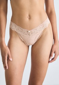 Woman wearing light pink lace panties with floral patterns, shown from waist to mid-thigh against a plain background.