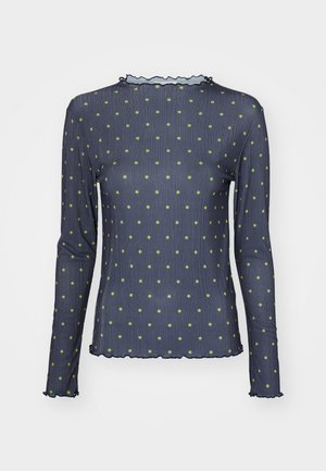 Long-sleeved top in dark blue, featuring green polka dots. Textured fabric with a ruffled neckline and hem. Form-fitting design.