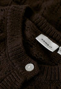 Maglione marrone lavorato a maglia con un motivo testurizzato, dotato di collo rotondo, colletto a coste e un bottone trasparente vicino all'etichetta.