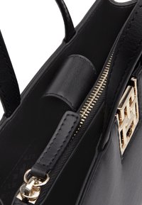 Bolso de mano de cuero negro con un logotipo de hardware en tono dorado, bolsillo con cremallera y detalles interiores. Presenta una textura suave y un diseño estructurado.