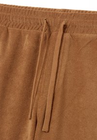 Pantalones deportivos marrones con una superficie texturizada, que cuentan con una cinturilla acanalada y cordón. El material parece suave y similar a forro polar.