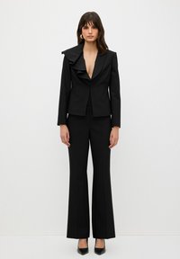 Zwarte op maat gemaakte blazer met een gerimpelde kraag, gecombineerd met bijpassende flared broek. Glad materiaal, aansluitend ontwerp, minimale hardware.