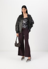 Black leather bomber jacket, graphic top with floral design, burgundy wide-leg striped trousers, silver shoes, small dark bag.