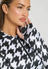 Pullover a maniche lunghe in motivo pied de poule bianco e nero con colletto a mezza zip e maniche con polsino; tessuto liscio e elasticizzato.