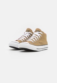 Tan canvas höga sneakers med vita snörning och gummisulor. Har svart rand vid sulan och logotyp på tungan.