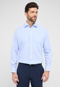 Lichtblauw hemd met lange mouwen en een button-down kraag, één borstzak en zilveren knopen, gecombineerd met donkerblauwe broek.